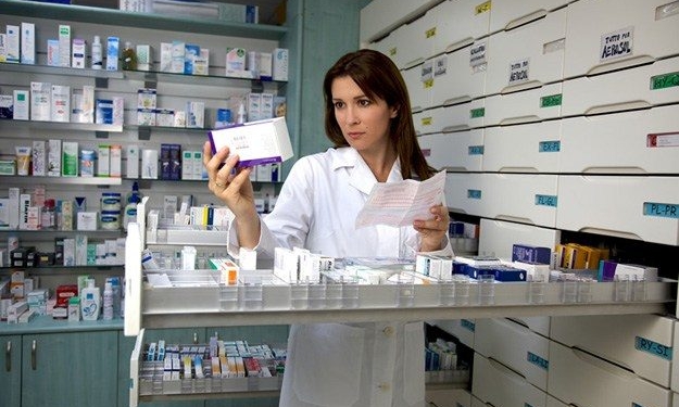 Beautiful female model pharmacist looking at medicine