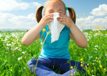 Little girl is blowing her nose while sitting on green meadow