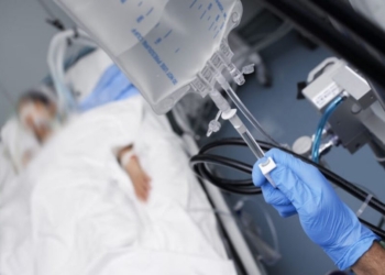 Male person with gloved hand turns off the intravenous drug system to the unconscious patient.