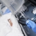 Male person with gloved hand turns off the intravenous drug system to the unconscious patient.