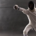 Boy wearing white fencing costume and black fencing mask standing with the sword practicing in fencing.