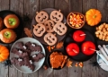 Rustic Halloween treat table scene over a dark wood background. Top view. Variety of candied apples, cookies, candy and sweets.