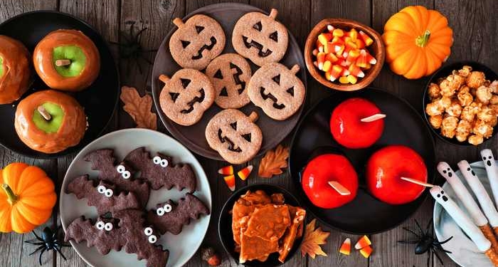 Rustic Halloween treat table scene over a dark wood background. Top view. Variety of candied apples, cookies, candy and sweets.