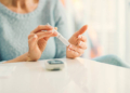 Mature woman doing blood sugar test at home in a living room. Selective focus to her finger.