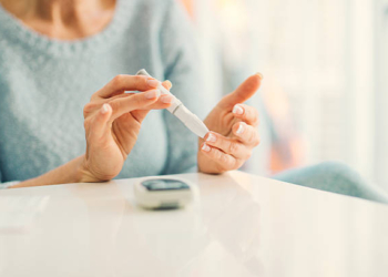 Mature woman doing blood sugar test at home in a living room. Selective focus to her finger.
